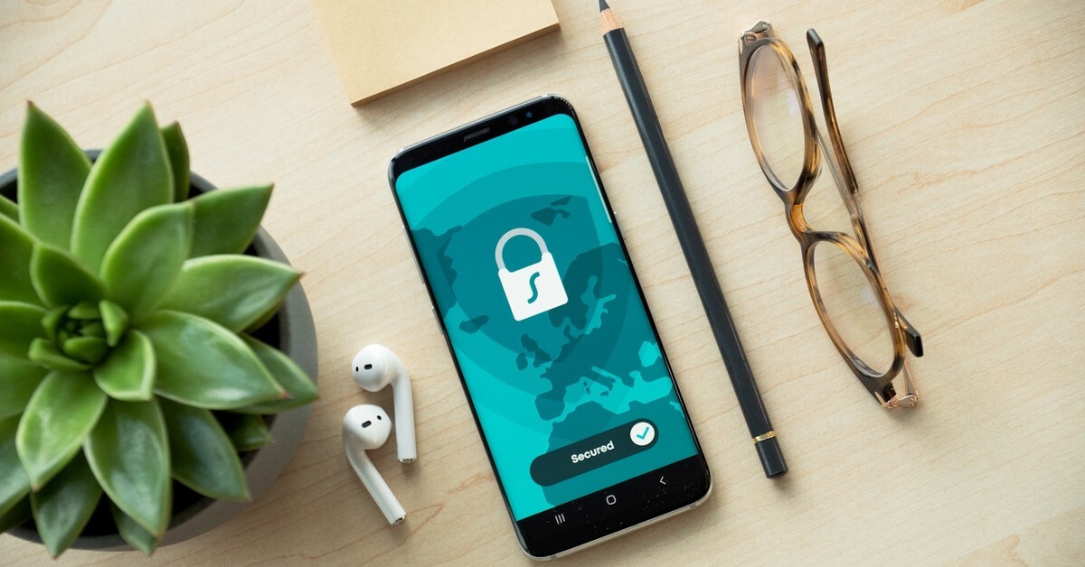 A smartphone displaying a secure connection screen on a wooden desk with glasses, a succulent plant, and AirPods nearby — representing mobile app authentication and OAuth security.