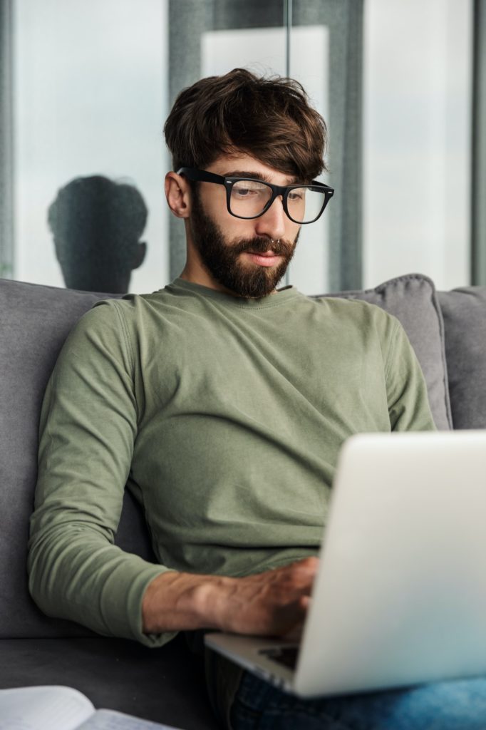 image-of-focused-bearded-man-working-with-laptop-while-sitting-on-sofa-682x1024